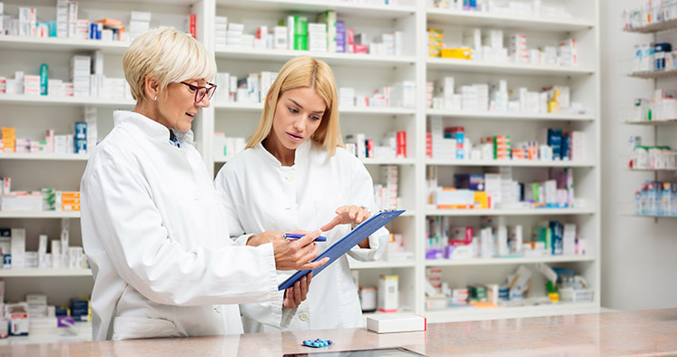 Mature and young female pharmacists working together, standing b